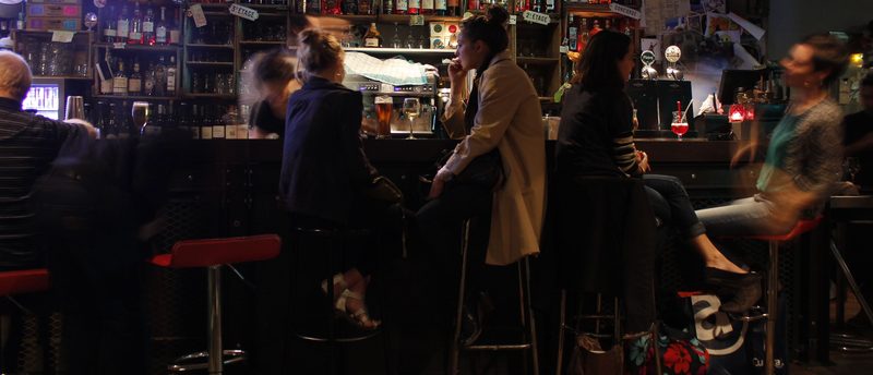 Clientes sentados no balcão de um bar cheio à noite